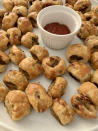 A platter of sausage rolls with a bowl of dipping sauce in the center