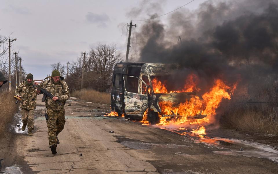 Ukrainian soldiers pass by a volunteer bus burning after a Russian drone strike near Bakhmut in Donetsk