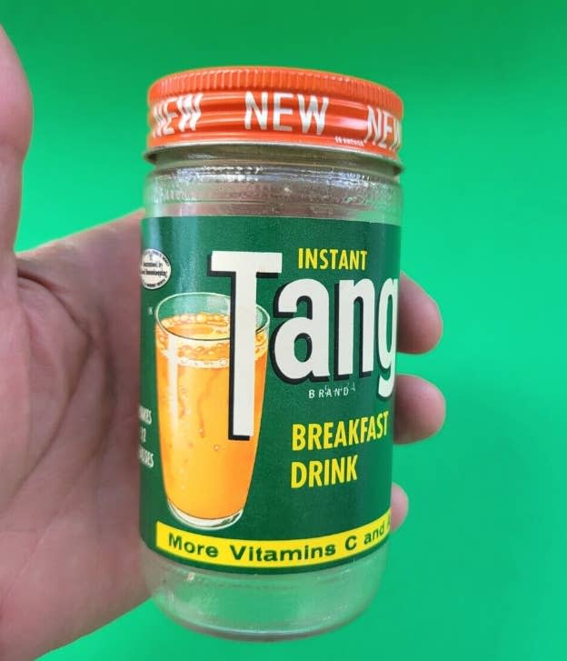 A hand holds a jar of Tang Instant Breakfast Drink, with a label showcasing a glass of the orange beverage and text highlighting vitamins C and D