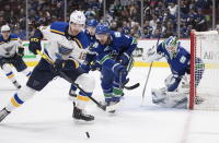 St. Louis Blues' Zach Sanford (12) reaches for the puck while being watched by Vancouver Canucks' Chris Tanev (8) in front of goalie Thatcher Demko (35) during the first period of an NHL hockey game in Vancouver, British Columbia on Monday Jan. 27, 2020. (Darryl Dyck/The Canadian Press via AP)