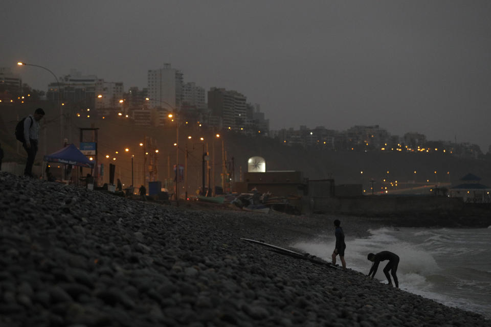 Surfers climb up rocky Makaha beach in Lima, Peru, as they exit the water as darkness falls, Thursday, July 25, 2019. Today, dozens of schools teach locals and tourists from across the world how to ride waves at beaches with Hawaiian names in Lima's Miraflores district, while professional surfers from across the Americas prepare to compete when the sport is featured for the first time in the Pan Am Games in the Peruvian capital.(AP Photo/Rebecca Blackwell)