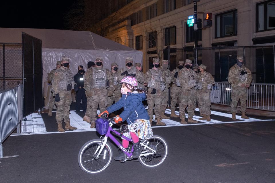 A small group of National Guardsmen look on as a local child cycles past.