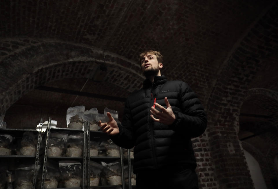 Hadrien Velge, a founding member of Le Champignon de Bruxelles, speaks with a journalist at the company's urban farm in the cellars of Cureghem in Brussels, Wednesday, Feb. 5, 2020. When the founding members of the company first tried to grow their Shiitake, Maitake and Nameko mushroom varieties using coffee grounds as a substrate, they realized the fungi much preferred organic beer waste. (AP Photo/Virginia Mayo)
