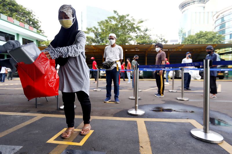 FILE PHOTO: People wearing protective face masks practice social distancing while receiving rice from an automated rice ATM distributor amid the spread of the coronavirus disease (COVID-19) in Jakarta