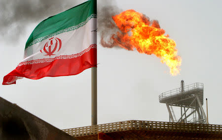 A gas flare on an oil production platform in the Soroush oil fields is seen alongside an Iranian flag in the Persian Gulf, Iran, July 25, 2005. REUTERS/Raheb Homavandi/Files