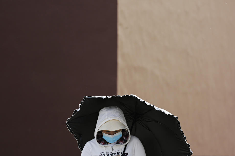 A woman wearing a face mask to help curb the spread of the coronavirus holds an umbrella while walking on a street in Beijing, Monday, April 26, 2021. (AP Photo/Andy Wong)