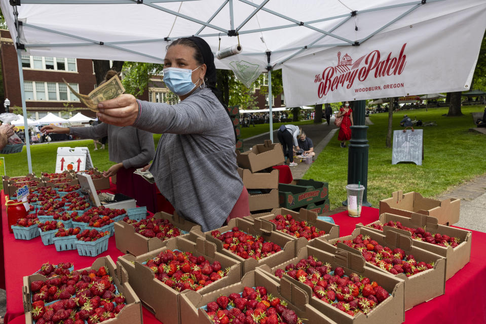 Nancy Sharabarin hands money to a customer buying strawberries at the Saturday farmers market as business opens up with a successful vaccination campaign in Portland, Ore., Saturday, June 5, 2021. Until a year ago, the city was best known nationally for its ambrosial food scene, craft breweries and “Portlandia” hipsters. Now, months-long protests following the killing of George Floyd, a surge in deadly gun violence, and an increasingly visible homeless population have many questioning whether Oregon’s largest city can recover. (AP Photo/Paula Bronstein)