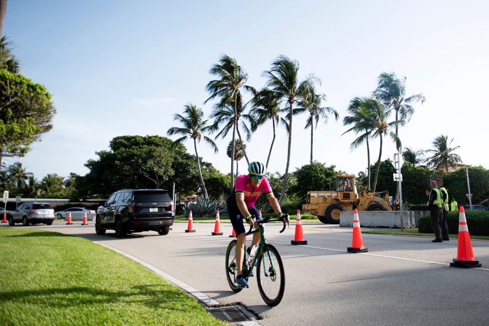 A cyclist heads south as members of the Florida Department of Transportation place concrete barriers near the roundabout on South Ocean Boulevard Saturday morning.  The barriers are being installed near the Mar-a-Lago Club as part of increased security measures to protect former President Donald Trump.