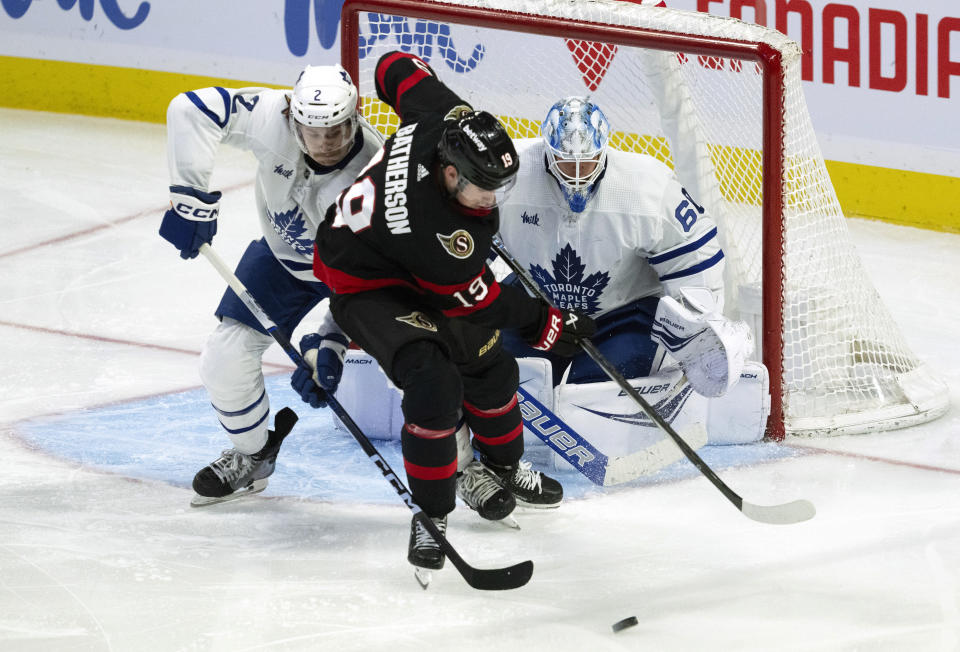 Ottawa Senators right wing Drake Batherson, cener, tries to control the puck under pressure from Toronto Maple Leafs defenseman Simon Benoit, left, as Male Leafs goaltender Joseph Woll, right, looks on during second-period NHL hockey game action Thursday, Dec. 7, 2023, in Ottawa. (Adrian Wyld/The Canadian Press via AP)