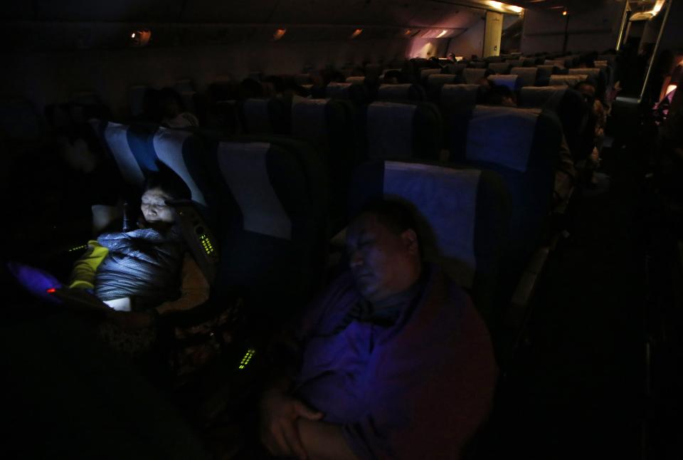 A Chinese passenger uses her tablet computer as other passengers sleep onboard Malaysia Airlines Boeing 777-200ER flight MH318 as it cruises towards Beijing over the South China Sea