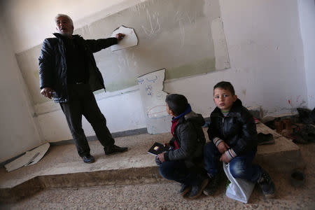 A teacher writes on a broken whiteboard during a class at the 'Aisha Mother of the BelieversÕ school which was recently reopened after rebels took control of al-Rai town from Islamic State militants, Syria January 17, 2017. Picture taken January 17, 2017. REUTERS/Khalil Ashawi