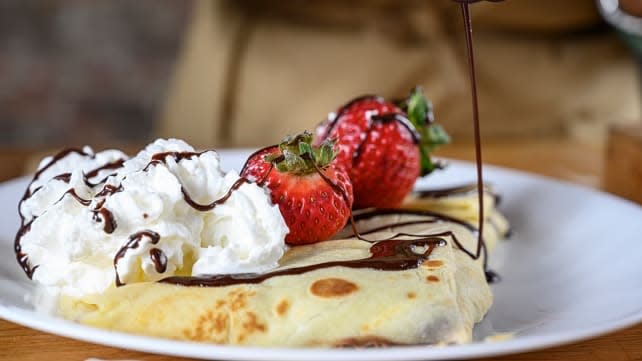 A crepe with whipped cream, strawberries and chocolate syrup.