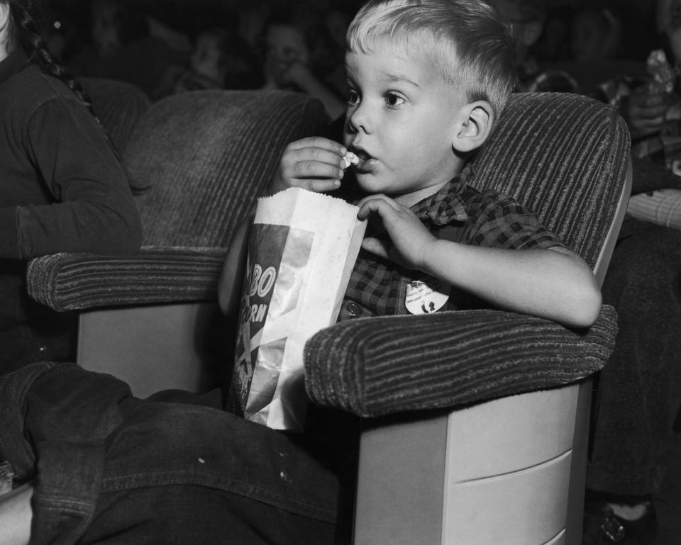 With eyes glued to the screen, a young boy eats a bag of popcorn while attending a Saturday matinee at the movie theater