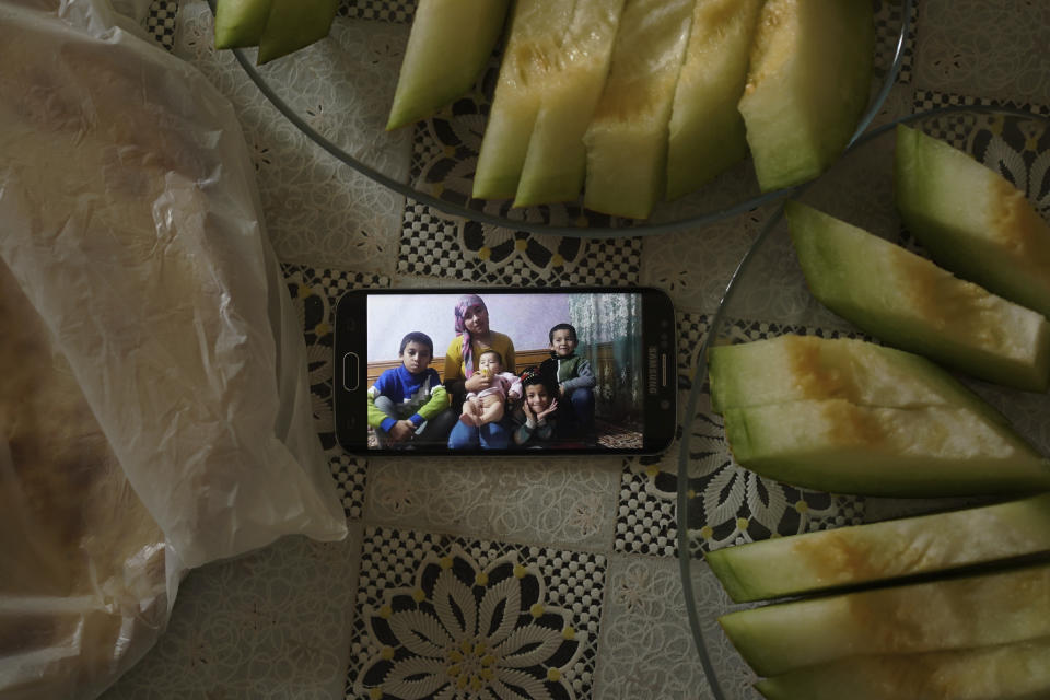 In this Aug. 23, 2018, photo, a phone displaying an image of the family of Adil, 42, father to five children and a businessman from Kashgar, China, sits on a table surrounded with bread and melons in Istanbul, Turkey . Adil got stuck in Turkey during a business trip after hearing that the Chinese government was seizing passports, and hasn't seen his children since. Three of his children were ordered to attend newly-built boarding schools in Kashgar and Turpan before he got stuck in Turkey. (AP Photo/Dake Kang)