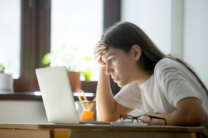 Young woman holding her head while looking at laptop.