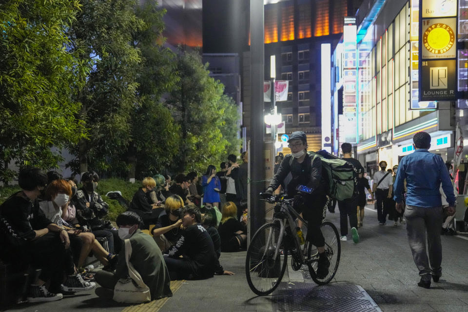 People walk around and gather at a bar after government imposed 8 p.m. closing time for restaurants and bars under Tokyo's fourth state of emergency Saturday, July 17, 2021, in Tokyo. The latest state of emergency has asked restaurants and bars to close by 8 p.m., if not entirely. This has pushed people to drink outside, although many bars remain open and bustling with customers who are defying the rules and expressing frustration and indifference. (AP Photo/Kiichiro Sato)