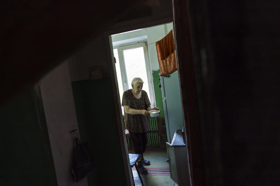 Ida Svystunova, 89, carries a bowl of soup to heat up on an electric plate in her damaged apartment from a May rocket attack in Sloviansk, Donetsk region, eastern Ukraine, Sunday, Aug. 7, 2022. Her son, Oleksandr, 69, brings her food and water daily as the city hasn't had running water in months. (AP Photo/David Goldman)