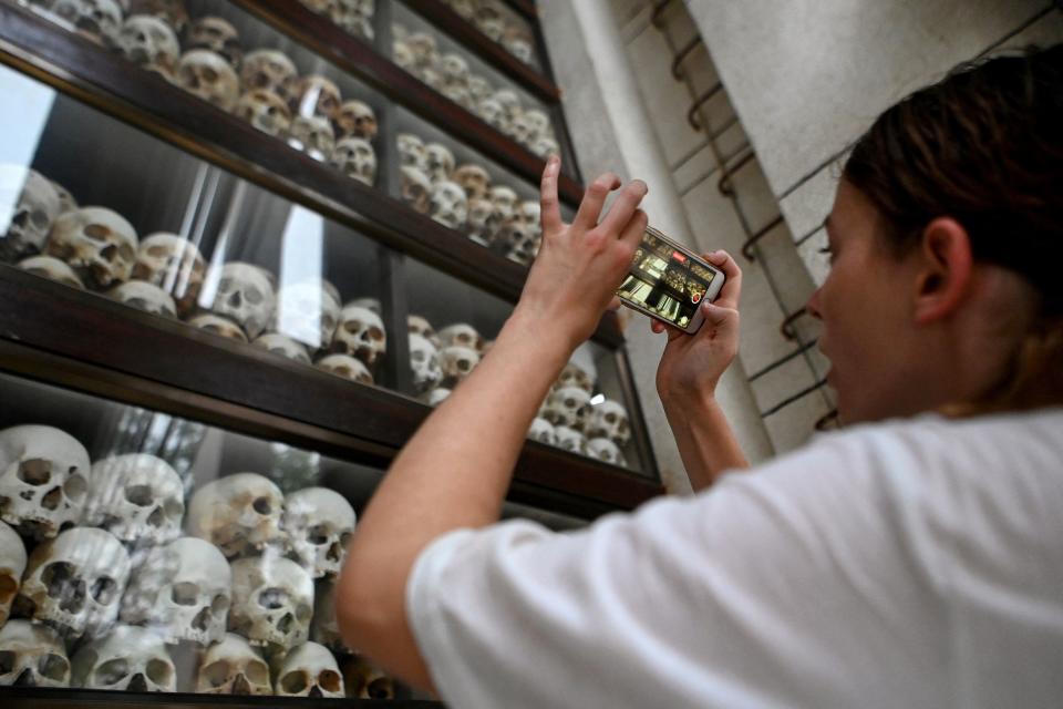 This photo taken on September 16, 2022, shows a tourist taking picture of skulls of victims of the Khmer Rouge regime at the Choeung Ek killing fields memorial in Phnom Penh. - Cambodia's UN-backed court set up to try Khmer Rouge leaders ends its work on September 22, but with just three convictions after 16 years' work the tribunal has brought only limited solace to survivors of the genocidal regime. - To go with package 'CAMBODIA-GENOCIDE-TRIBUNAL-UN' (Photo by TANG CHHIN Sothy / AFP) / To go with package 'CAMBODIA-GENOCIDE-TRIBUNAL-UN' (Photo by TANG CHHIN SOTHY/AFP via Getty Images)