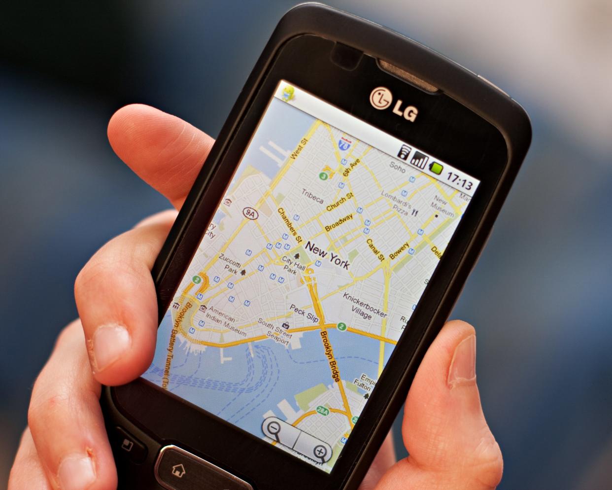 hand holding a smartphone with screen showing the Google maps app, satellite view of New York City