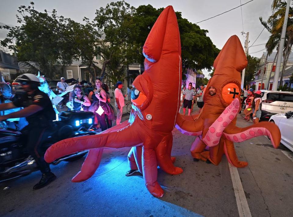 A police officer rides past two revelers costumed as squids during the Captain Morgan Masquerade March Friday, Oct. 27, 2023, in Key West.