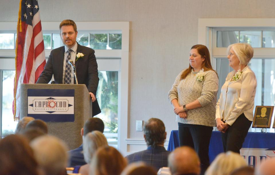 Brian Higgins, left, accepts the induction of his father, James Higgins, into the Cape Cod Baseball League Hall of Fame on Sunday at the Wequassett Resort and Golf Club. Higgins passed away earlier this year after serving 40 years in the league holding  different roles. His wife, Colleen, right, and his daughter, Courtney, shared the stage as Brian Higgins during the ceremony.