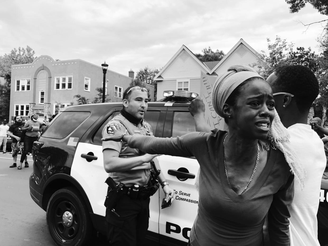 A woman with her arm outstretched stands near a police officer.