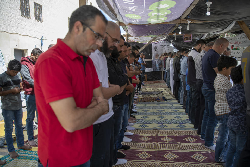 Palestinians attend Friday prayers next to a poster with picture and name of Mai Afaneh, who was shot dead by Israeli forces in the West Bank last June and held her body after, and reads "we promise to keep the path of struggle and build our independent state," at a sit-in tent for families of Palestinians killed in conflict and Israel is holding their bodies, in the village of Abu Dis, South of Ramallah, Friday, Sept. 24, 2021. (AP Photo/Nasser Nasser)