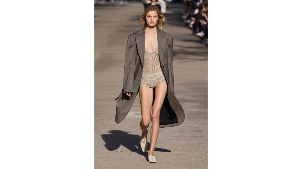 A model wears sequin micro shorts and a long grey coat at Stella McCartney SS24