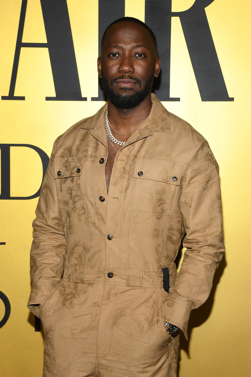 lamorne morris, a man stands with hands in his pockets wearing a brown jumpsuit