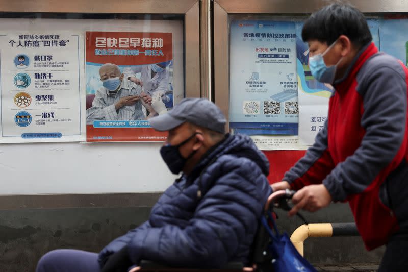 People pass by a poster encouraging elderly people to get vaccinated against COVID-19, in Beijing