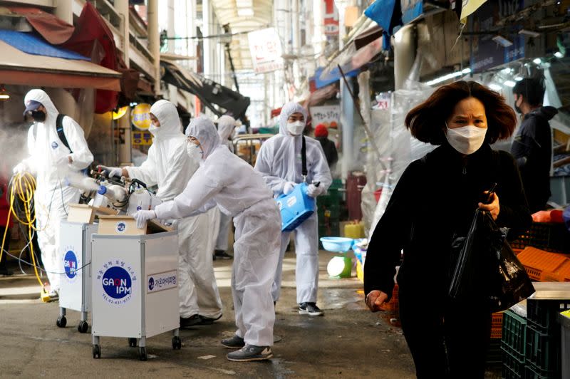 FILE PHOTO: A woman wearing a mask to prevent contracting the coronavirus reacts as employees from a disinfection service company sanitize a traditional market in Seoul