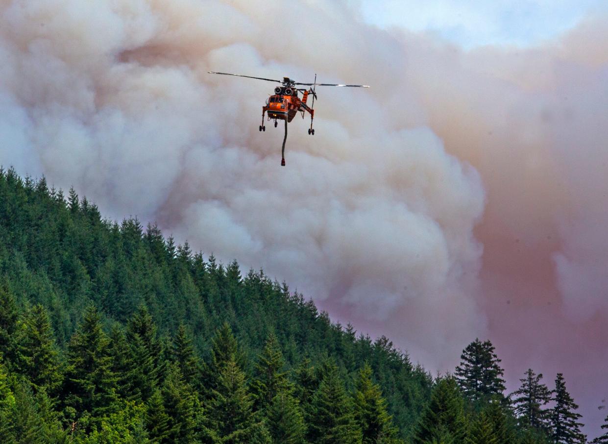 A helicopter flies between the Bedrock Fire and nearby Fall Creek to get a load of water as the wildfire burns east of Eugene on Monday.