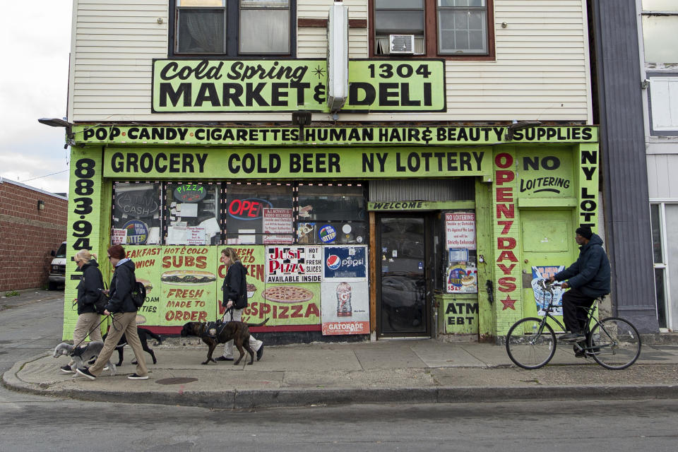 People walk dogs and bike near Cold Spring Market on Deli on Jefferson Avenue on Tuesday, May 17, 2022, in Buffalo, N.Y. After decades of neglect and decline, only a handful of stores are now along Jefferson Avenue. (AP Photo/Joshua Bessex)