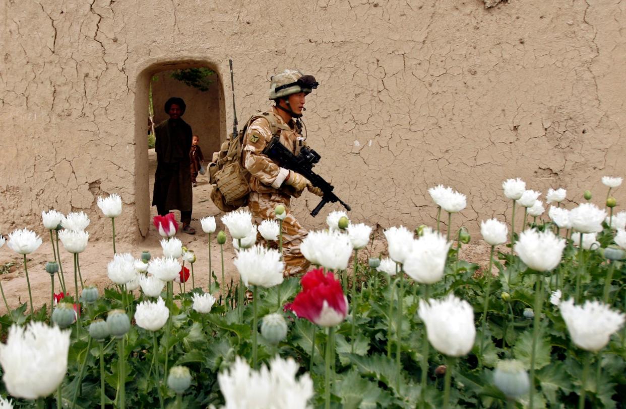 <span>An Afghan man watches a British soldier walking past a poppy field in Musa Qala, Helmand province, in 2009.</span><span>Photograph: Reuters</span>