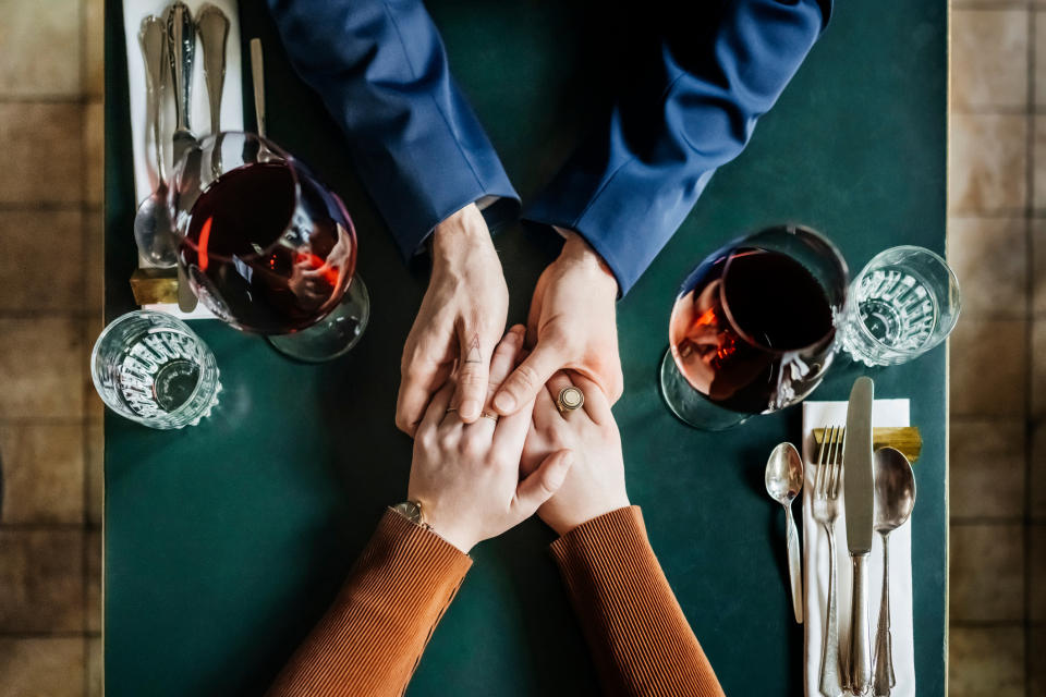 People holding hands at a table with wine