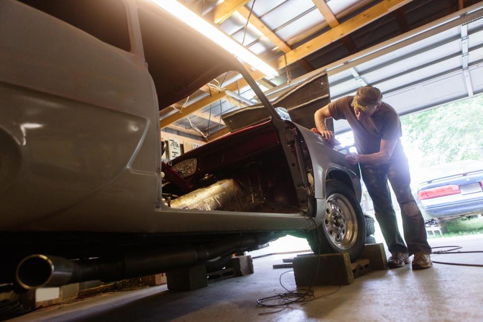 Older man working on car in home garage with door open. 