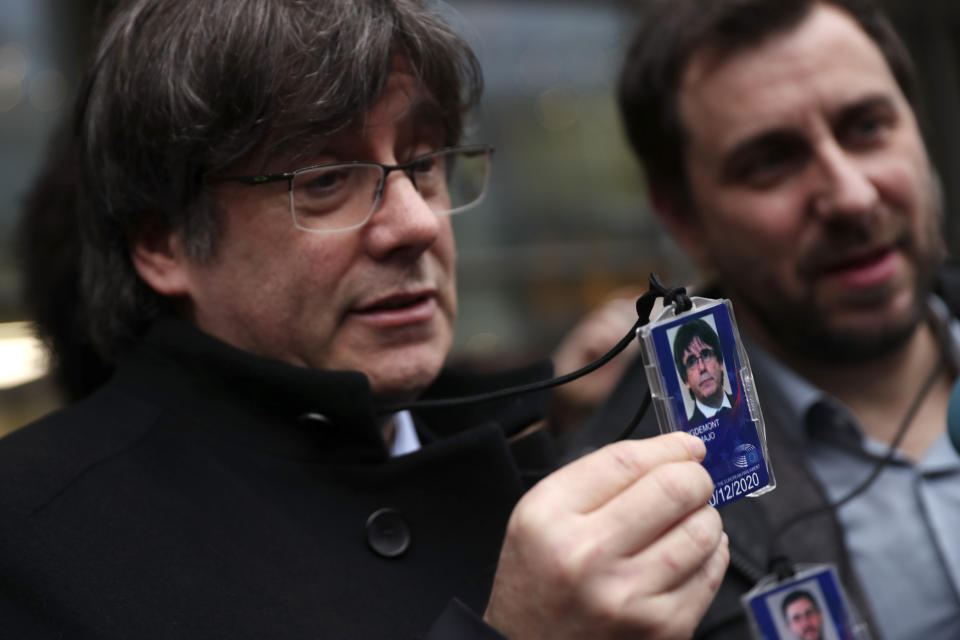 Catalonia's former regional president Carles Puigdemont, left, shows his accreditation badge as he stands next to former Catalan regional minister Antoni Comin outside the European Parliament in Brussels, Friday, Dec. 20, 2019. In a potentially stinging reversal for Spanish justice authorities, the European Union's top court ruled that a former Catalan official serving a prison sentence for his role in a banned independence referendum two years ago had the right to parliamentary immunity when he was on trial. (AP Photo/Francisco Seco)