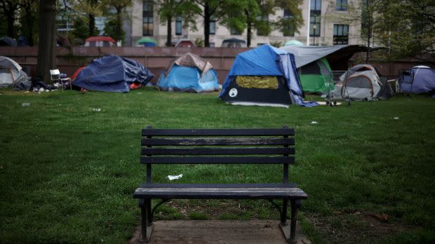 a group of four tents sits on the lawn of a park in Washington, DC, in front of a park bench