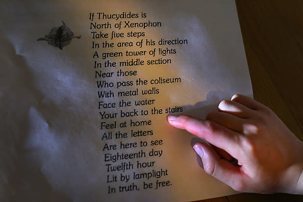 A person points at a map or parchment with a poem-like list of clues about directions and locations, mentioning Thucydides, Xenophon, and various landmarks