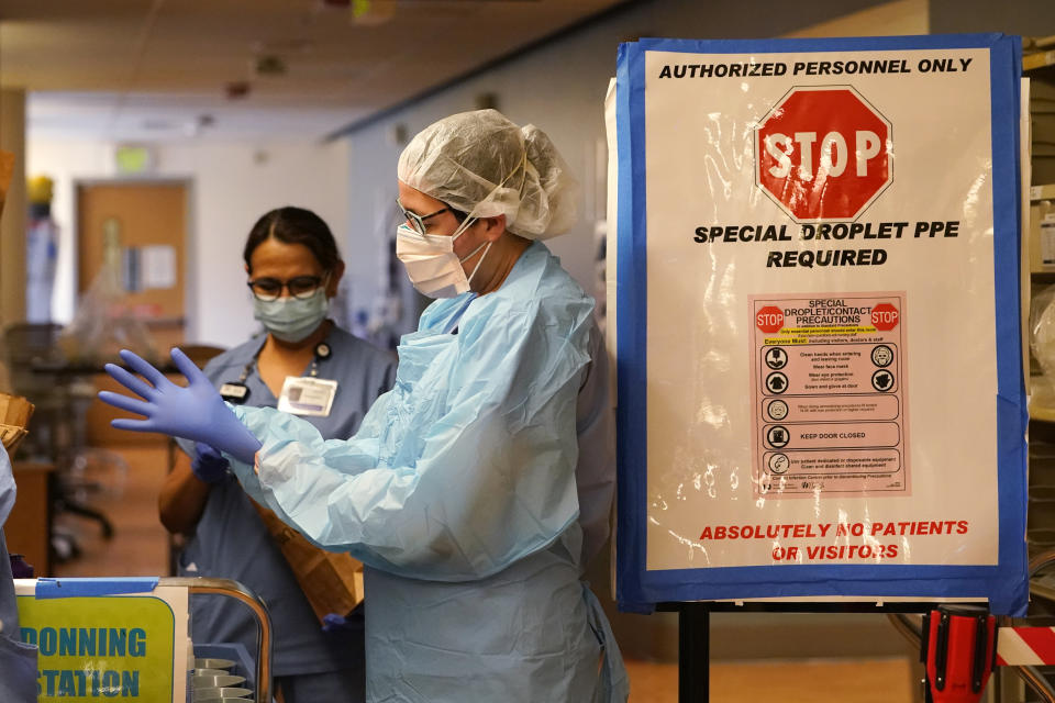 Registered nurse Diane Miller pulls on gloves and other protective equipment as she prepares to enter patient rooms in the COVID acute care unit at UW Medical Center-Montlake, Tuesday, Jan. 26, 2021, in Seattle. King County, where the hospital is located, has been on a downward trend of COVID-19 cases after two-and-a-half straight months of increases. But the current lull could be, and some experts believe will be, upended as more contagious variants of the virus spread throughout United States. (AP Photo/Elaine Thompson)