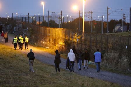 Migrants walk past a fence as another one (top R) tries to go in Eurotunnel freight shuttle near the Channel Tunnel access in Coquelles, near Calais, France, July 30, 2015. REUTERS/Pascal Rossignol