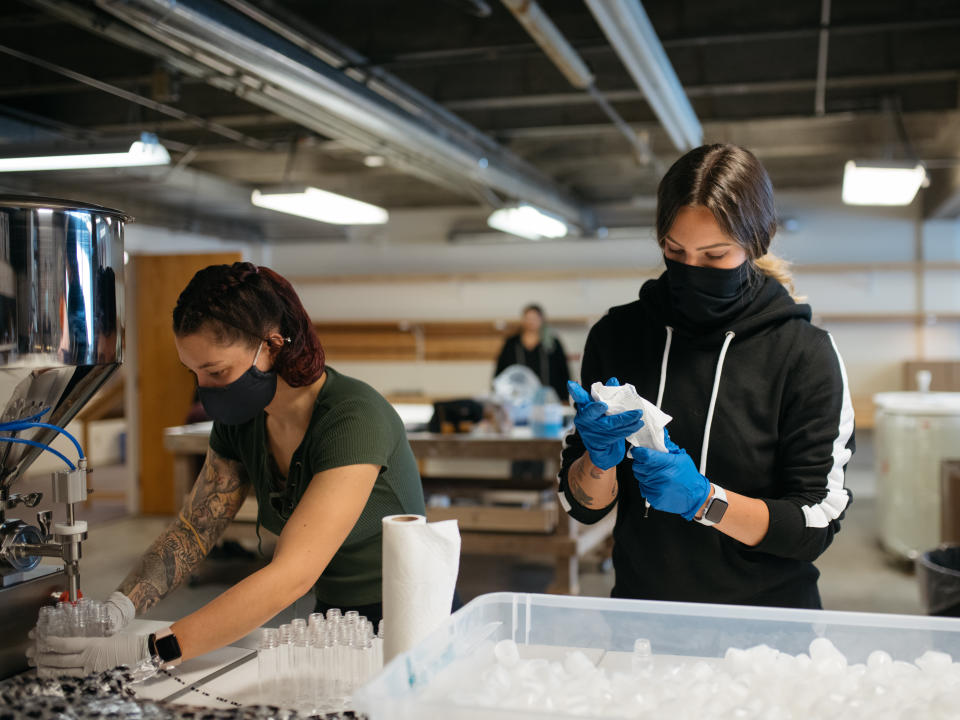 Amanda Halverson, left, fills bottles of hand sanitizer from a pneumatic filler while Makayla Deppa readies caps for the capping machine. (Photo: Grant Hindsley for HuffPost)