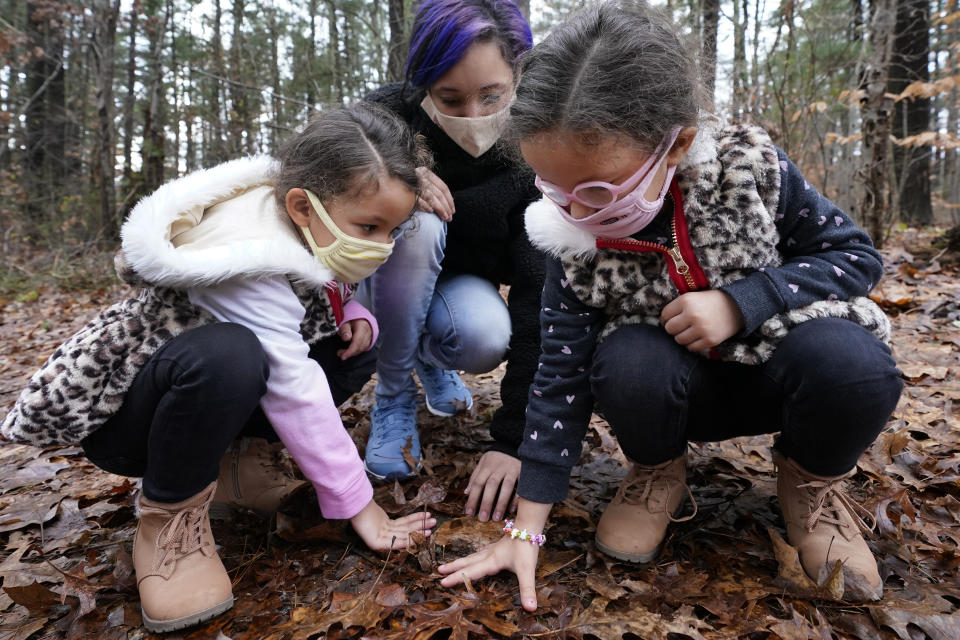 Mattakeeset Massachuset tribal members Shadia Fernandes-Dion, middle, and her four-year-old twin daughters, Anastasia, left, and Anaaliyah, right, touch the ground to honor their land at Titicut Indian Reservation, Friday, Nov. 27, 2020, in Bridgewater, Mass. A rift has been widening between Native American groups in New England over a federal reservation south of Boston where one tribe is planning to build a $1 billion casino. The Mattakeeset Massachuset tribe contend the Mashpee Wampanoag tribe doesn't have exclusive claim to the lands under their planned First Light casino in the city of Taunton, as they've argued for years. (AP Photo/Elise Amendola)