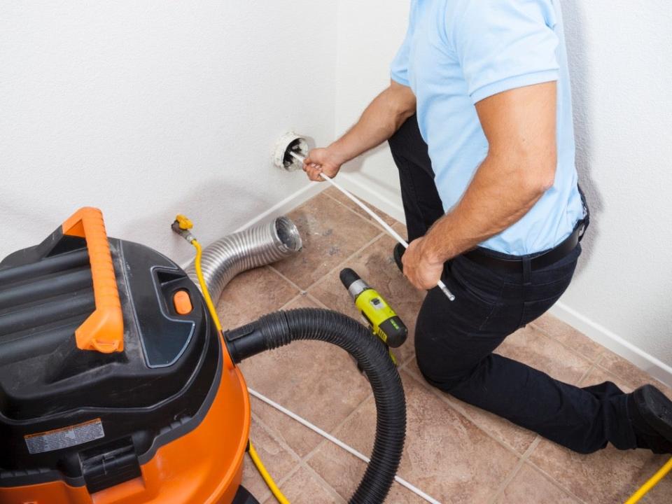 Man cleaning dryer vent in home with shop vac nearby