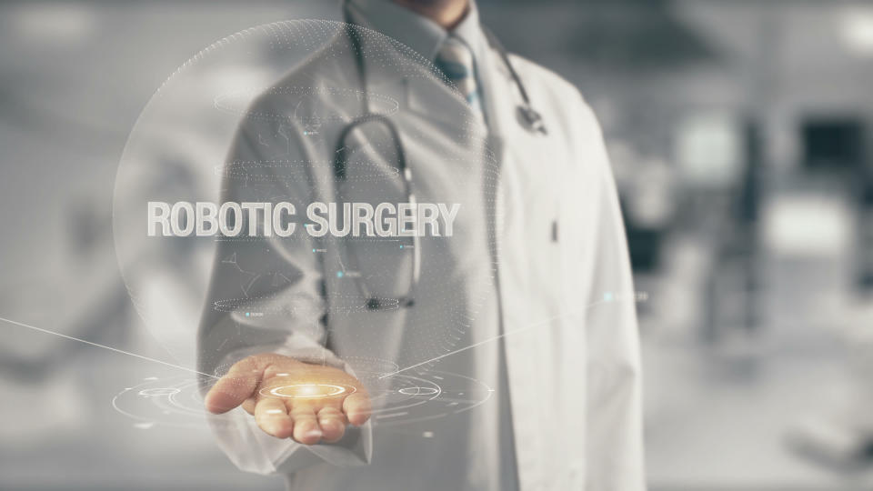 Physician with stethoscope around neck and palm extended beneath a computer-generated image with the words "robotic surgery."