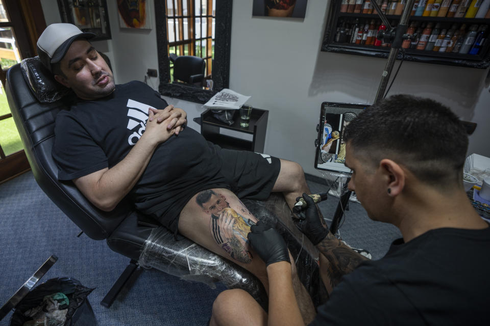 Artist César "Yeyo" Molina tattoos Sebastian Fernandez's leg, featuring a large image of soccer player Lionel Messi with the World Cup trophy, in Buenos Aires, Argentina, Thursday, Dec. 29, 2022. (AP Photo/Victor R. Caivano)