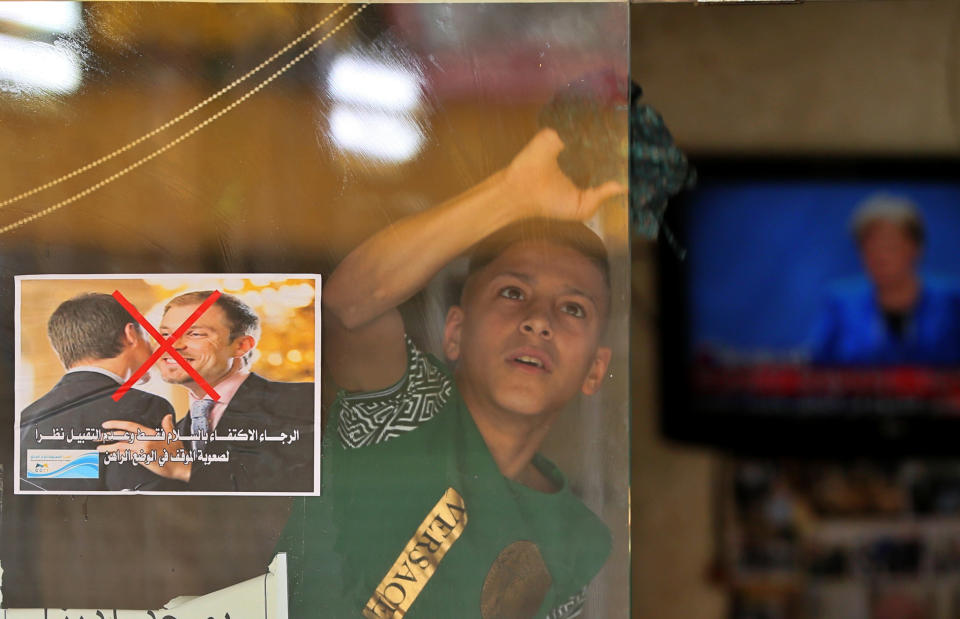 File - In this Thursday, March 19, 2020 file photo, a young worker cleans the window of a barbershop that posts a warning sign referring to the coronavirus, with Arabic that reads, "Please greet only and don't kiss, due to the difficult circumstances in the current situation," in Baghdad, Iraq. Iraq announced a weeklong curfew to help fight the COVID-19 pandemic. (AP Photo/Hadi Mizban, File)