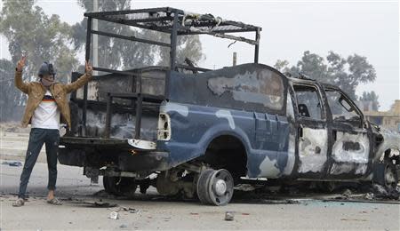 A protester stands next to the wreckage of a police vehicle in Ramadi December 30, 2013.REUTERS/Ali al-Mashhadani