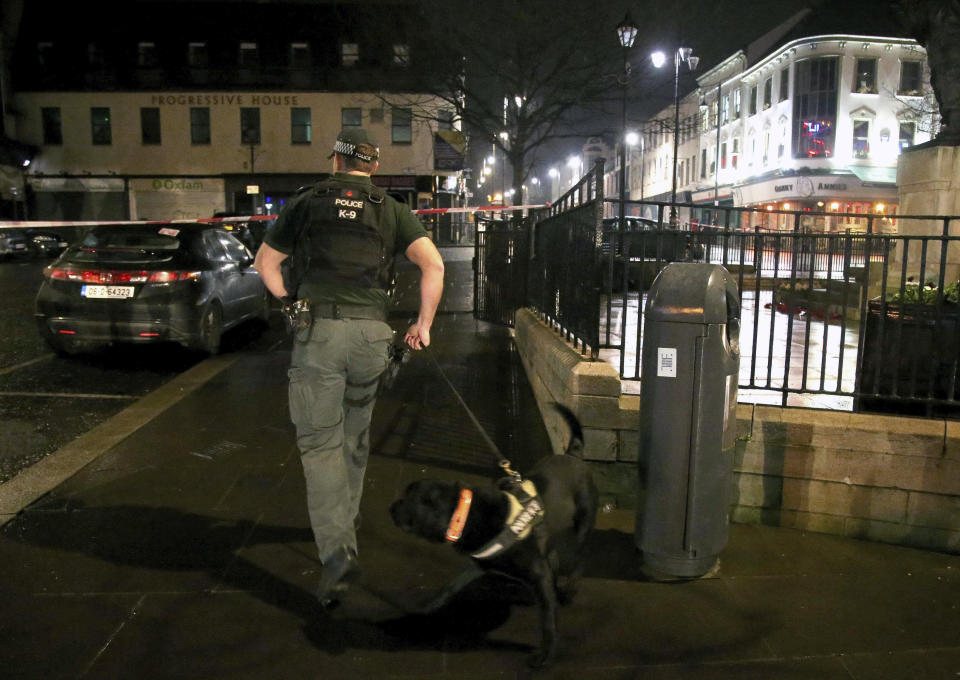 In this photo taken on Saturday, Jan. 19, 2019, a police officer with a sniffer dog are near the scene of a suspected car bomb on Bishop Street in Londonderry, Northern Ireland. Northern Ireland politicians are condemning a car bombing outside a courthouse in the city of Londonderry. The device exploded Saturday night as police, who had received a warning, were evacuating the area. The Police Service of Northern Ireland posted a photograph of a vehicle in flames and urged the public to stay away. (Steven McAuley/PA via AP)