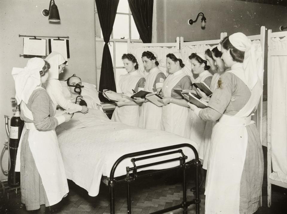 Student nurses taking notes around a patient’s bed, whilst a sister tutor explains the use of an oxygen mask, at Hope Hospital, Salford